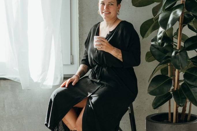 Die Frau sitzt mit einem Kaffee in der Hand und präsentiert sich im schwarzen Morgenmantel.