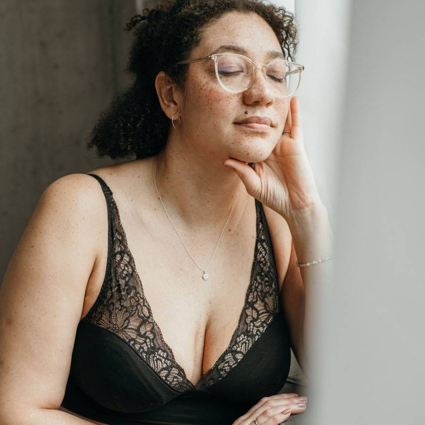 Moodbild vom Sophie Bralette in schwarz, das Model sitzt am Fenster und träumt vor sich hin.