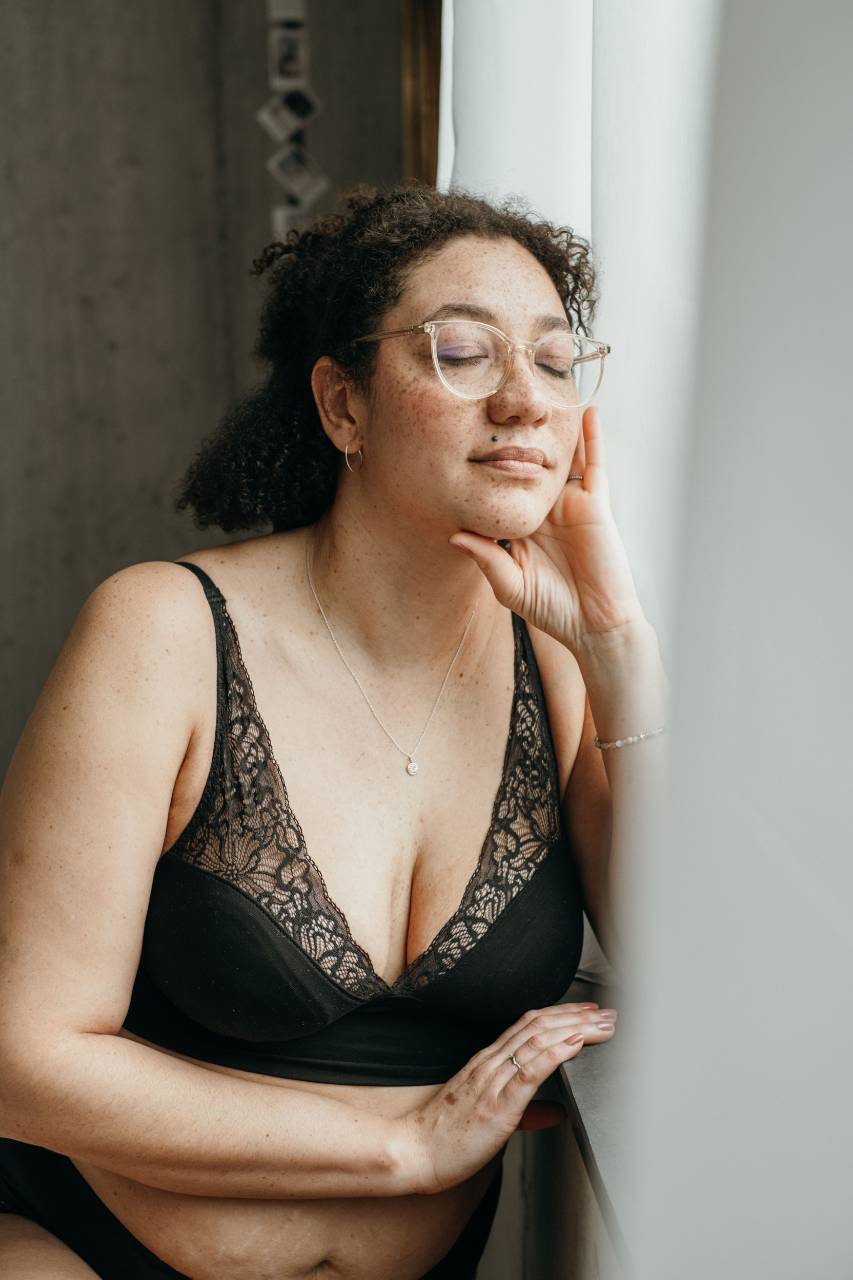 Moodbild vom Sophie Bralette in schwarz, das Model sitzt am Fenster und träumt vor sich hin.