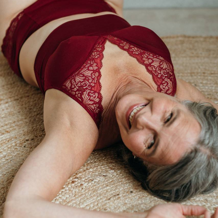 Moodbild von Sophe in Ruby Red. Model liegt auf dem Rücken und lächelt in die Kamera.