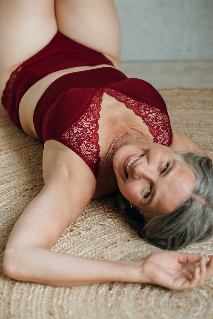 Moodbild von Sophe in Ruby Red. Model liegt auf dem Rücken und lächelt in die Kamera.