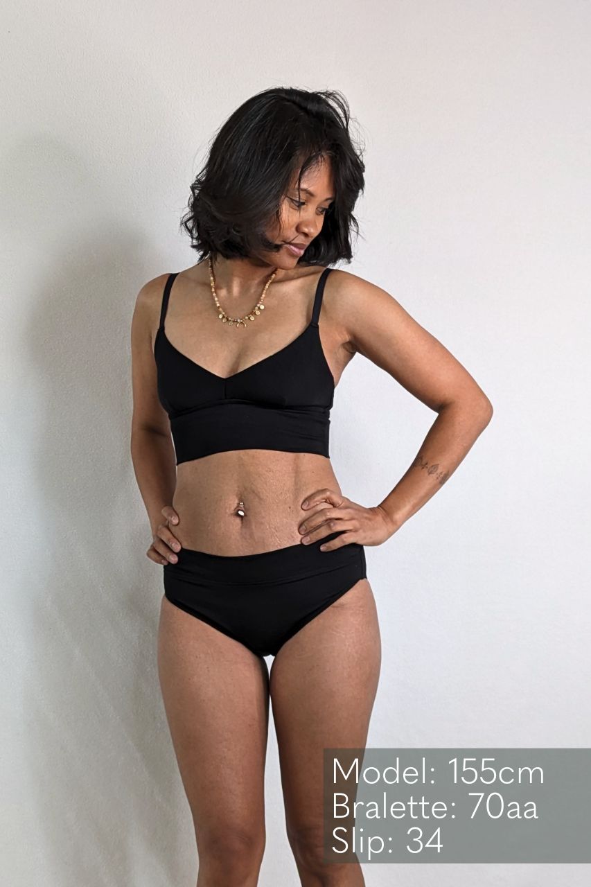 Le modèle appuie ses mains sur ses hanches de et pose dans un ensemble Emma composé de Bralette et d'un slip.