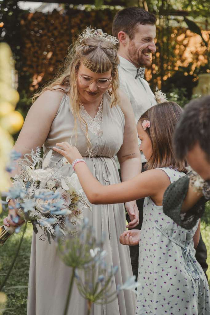 Braut in weissem Kleid und hervorblitzenden Bralette mit Kindern und Blumen