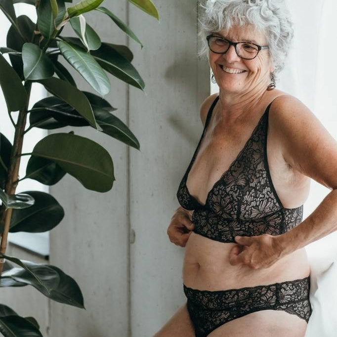 Femme adossée à un rebord de fenêtre devant un rideau blanc, en lingerie noire.