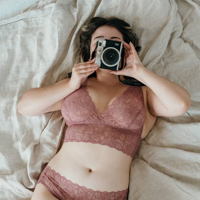 Femme allongée sur un lit et prenant une photo avec un appareil Polaroid
