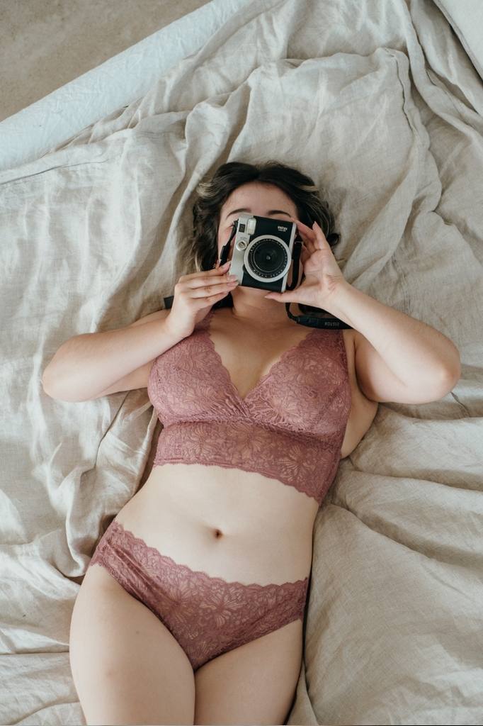 Frau liegt auf Bett und macht ein Foto mit Polaroid Kamera