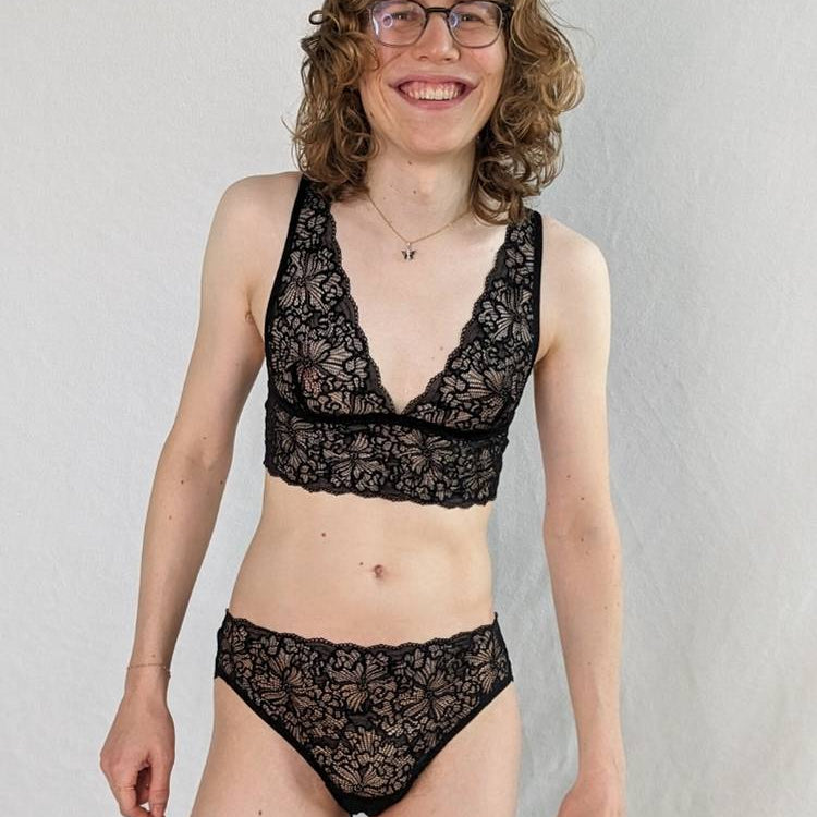 Femme debout sur un fond blanc en Bralette noir et Slip en dentelle.