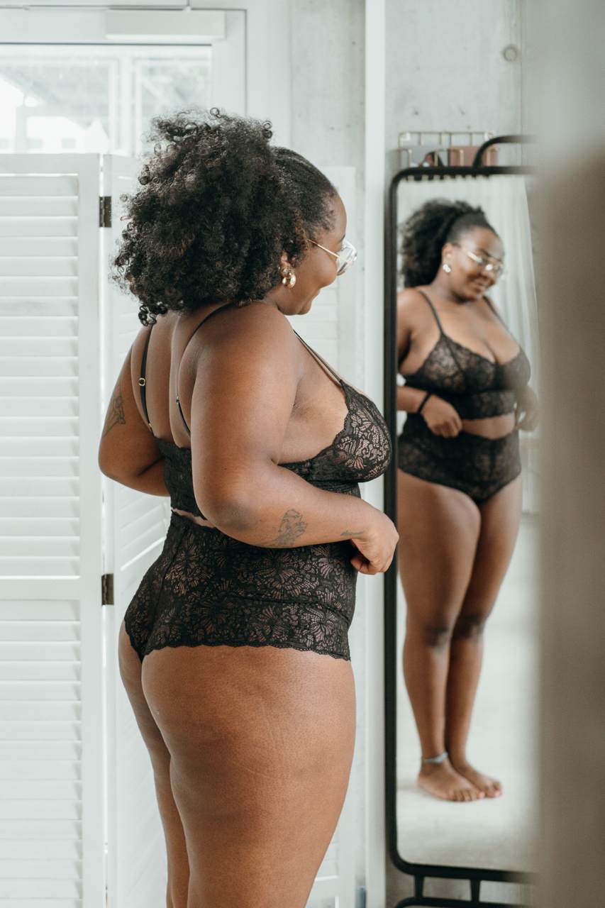 Frau in nachhaltiger Spitzenunterwäsche in schwarz betrachtet sich im Spiegel