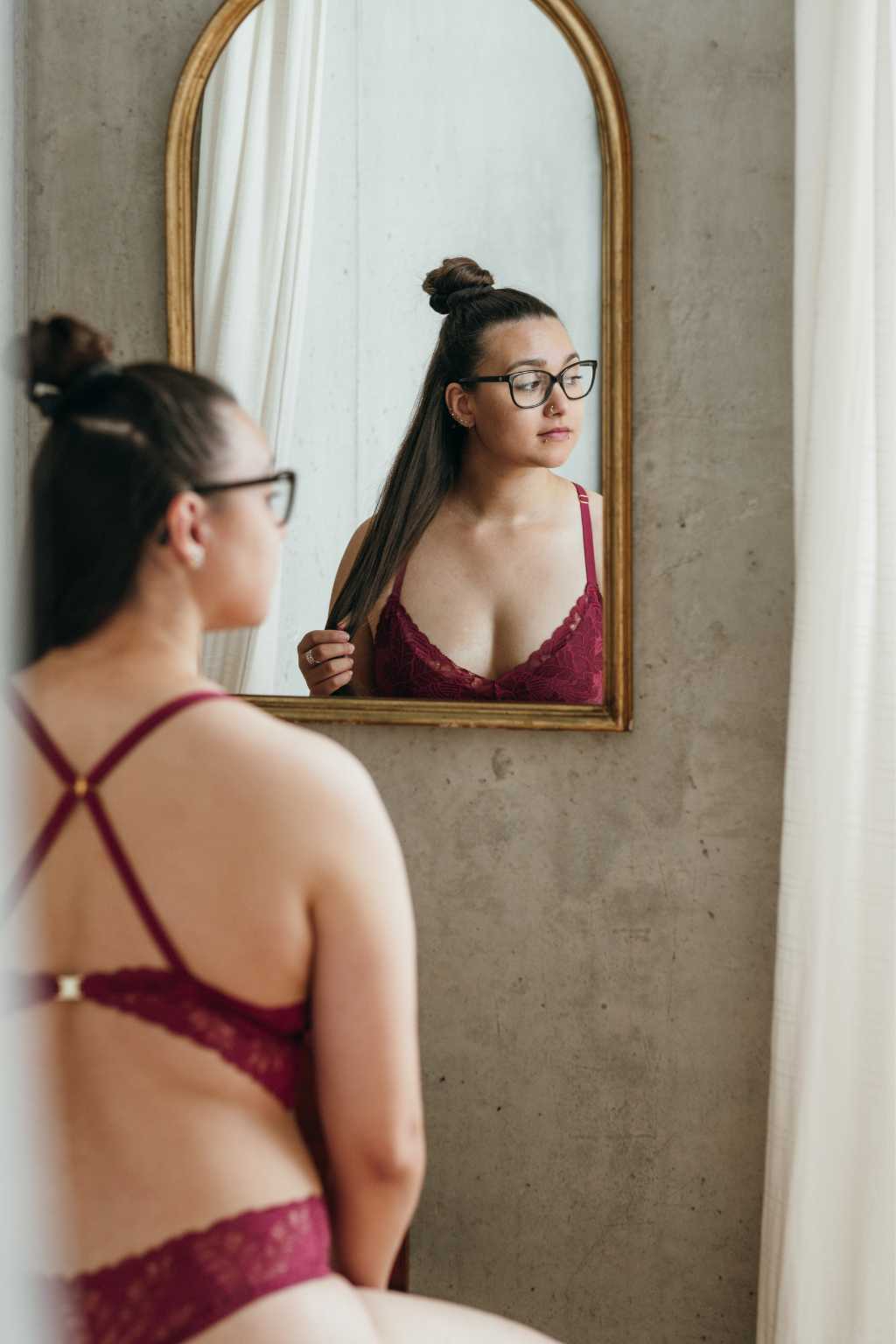 Boudoir Shooting - Frau trägt rote Spitzenunterwäsche und schaut in den Spiegel