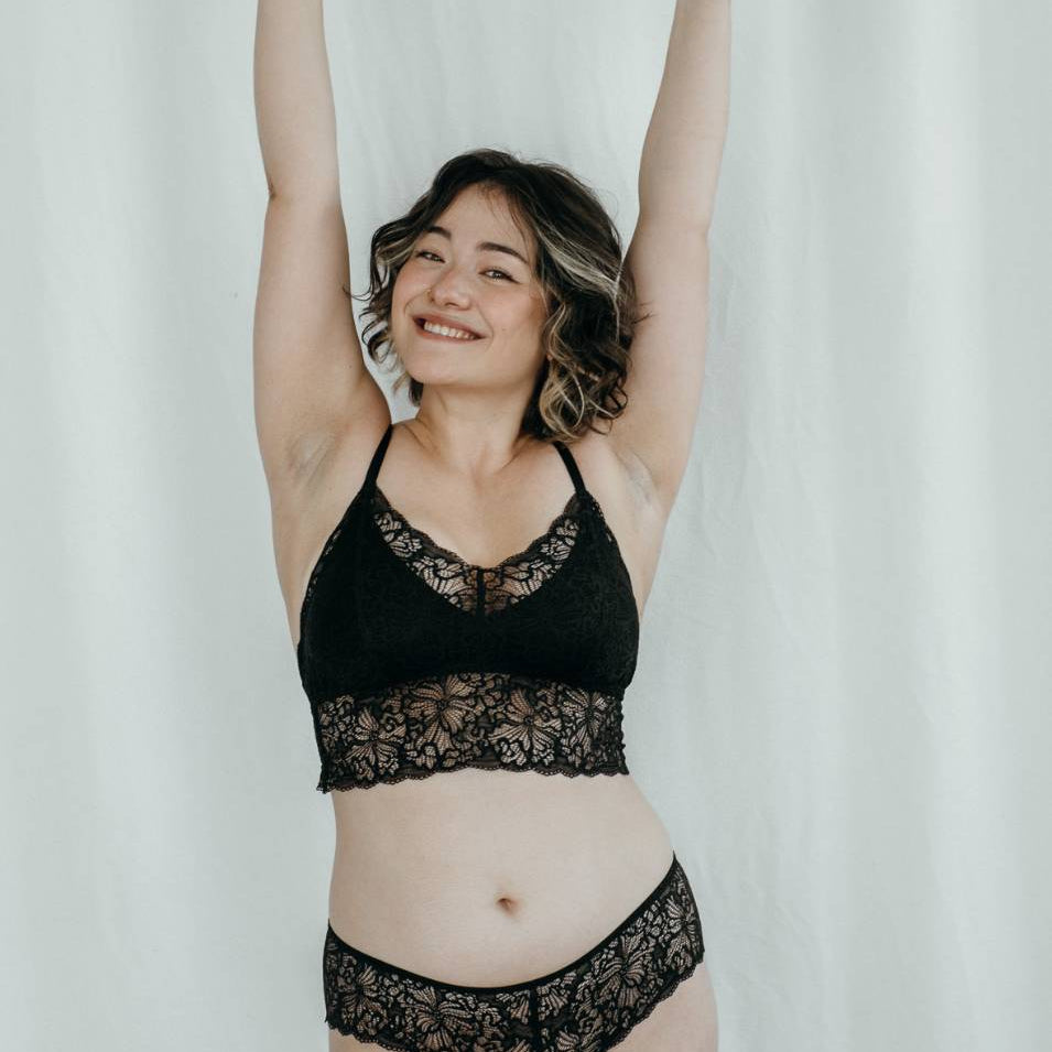 Modèle en Bralette et Slip en dentelle tend les mains en l'air.