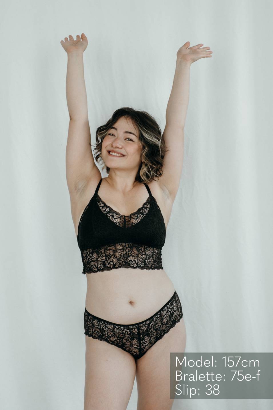 Modèle en Bralette et Slip en dentelle tend les mains en l'air.