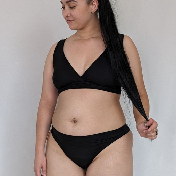 Jeune femme portant de la lingerie noire en String et Bralette, qui est croisée sur le devant.