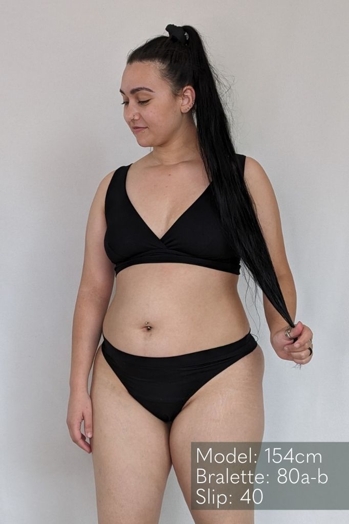 Jeune femme portant de la lingerie noire en String et Bralette, qui est croisée sur le devant.