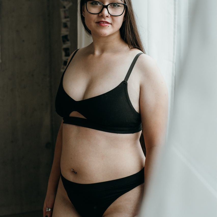Lors d'un shooting boudoir, le modèle se tient en lingerie noire devant un rideau blanc.