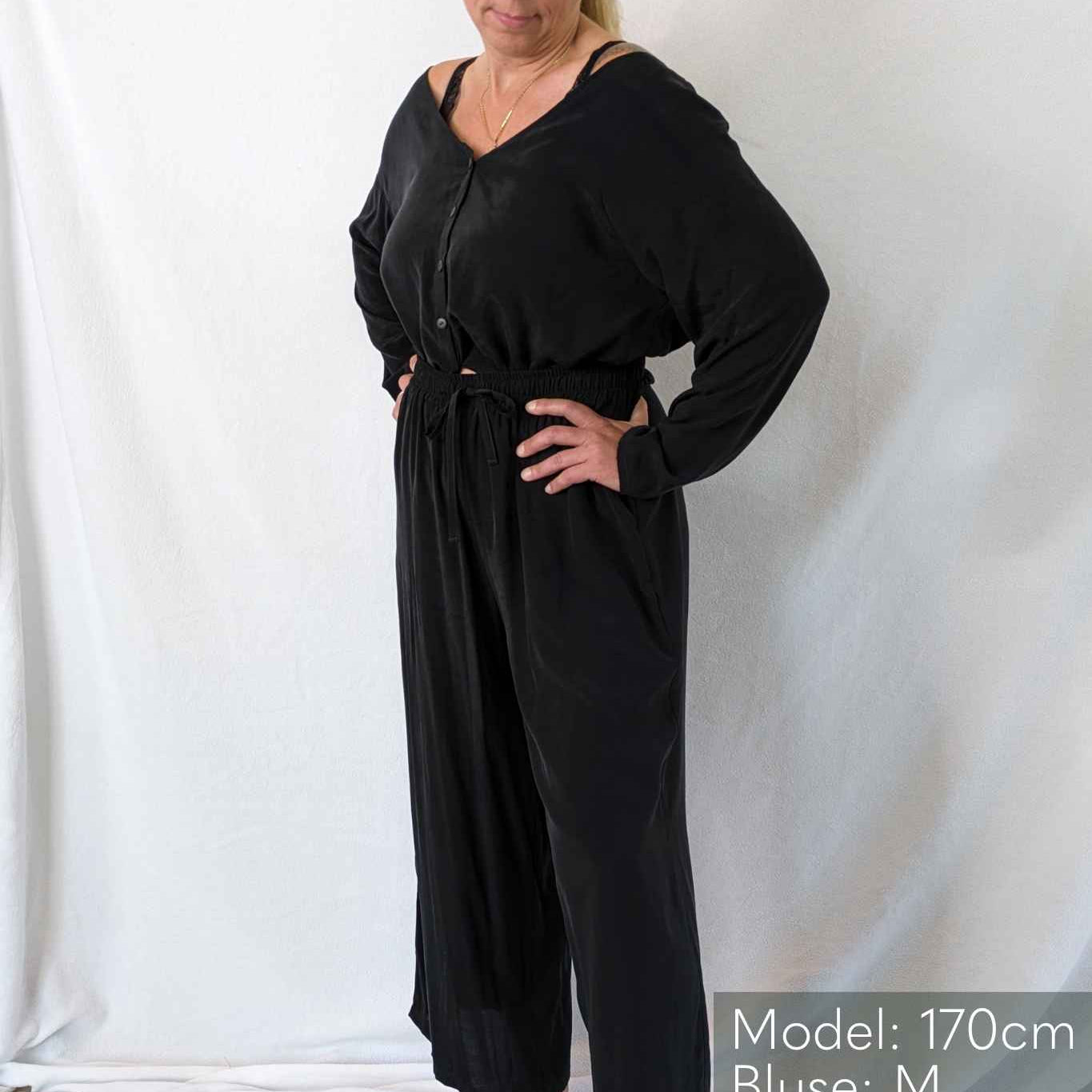 Une femme porte un pyjama noir sur un fond blanc.