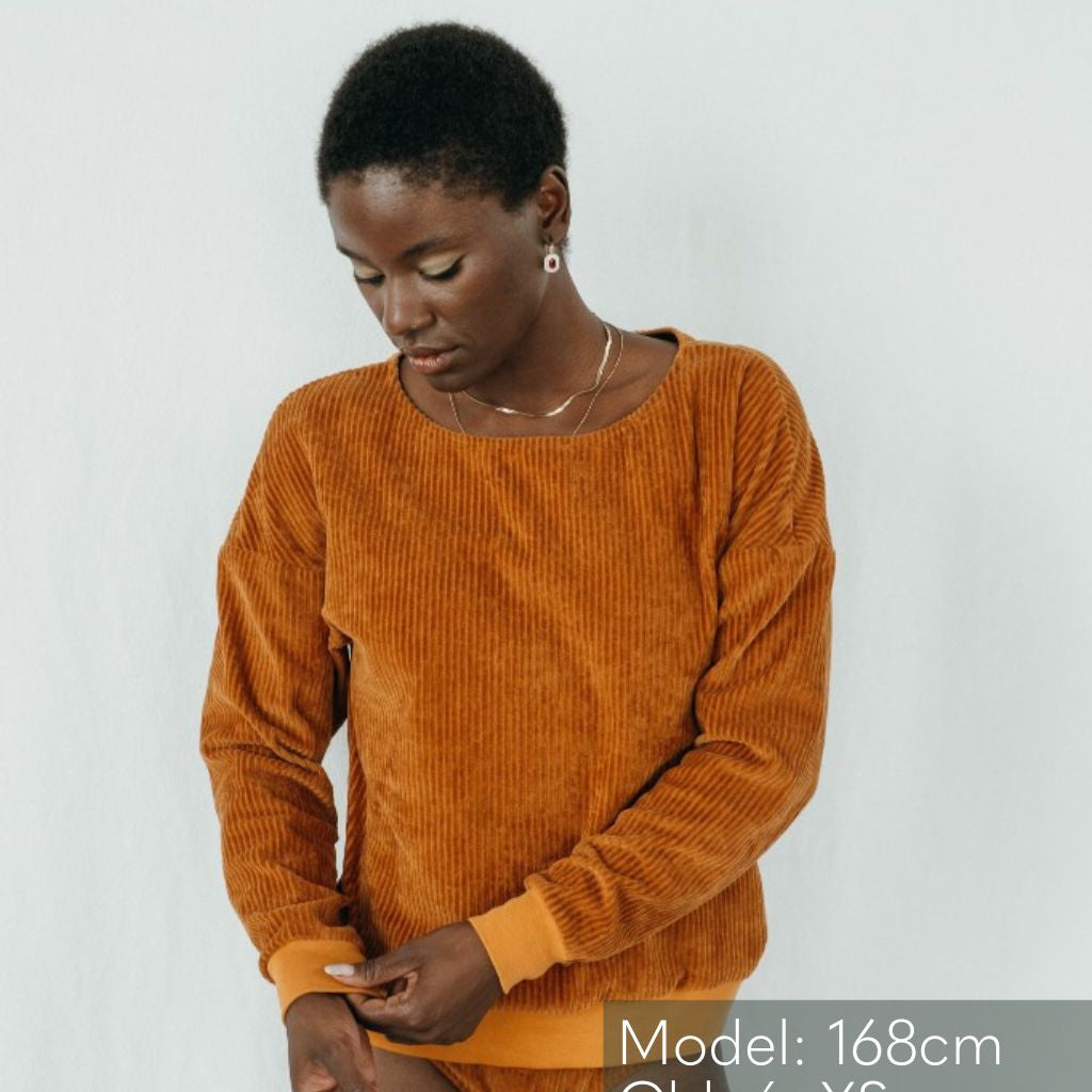 Model vor weissem Hinterdrund trägt Pulli in Ocker und zieht am Bündchen