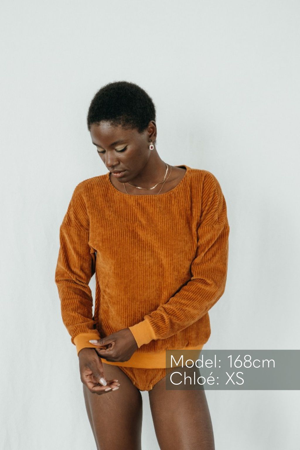 Model vor weissem Hinterdrund trägt Pulli in Ocker und zieht am Bündchen