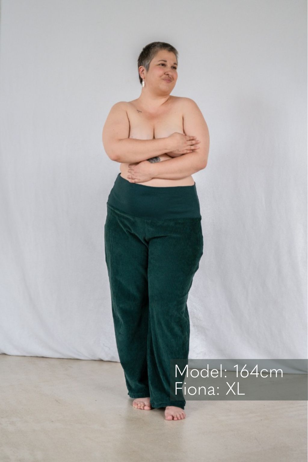 Frau mit kurzen Haaren hält sich die Brust und trägt hochgeschnittene Samt-Hose in Dunkelgrün