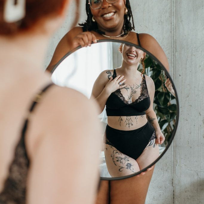 die Frau sieht sich im Spiegel im Alison Set in schwarz, die eine ander Frau hält