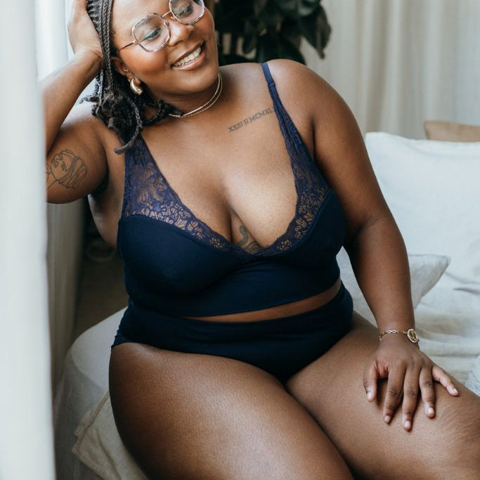 die sitzende Frau lacht und präsentiert ein Dessous in blau aus Top und Höschen