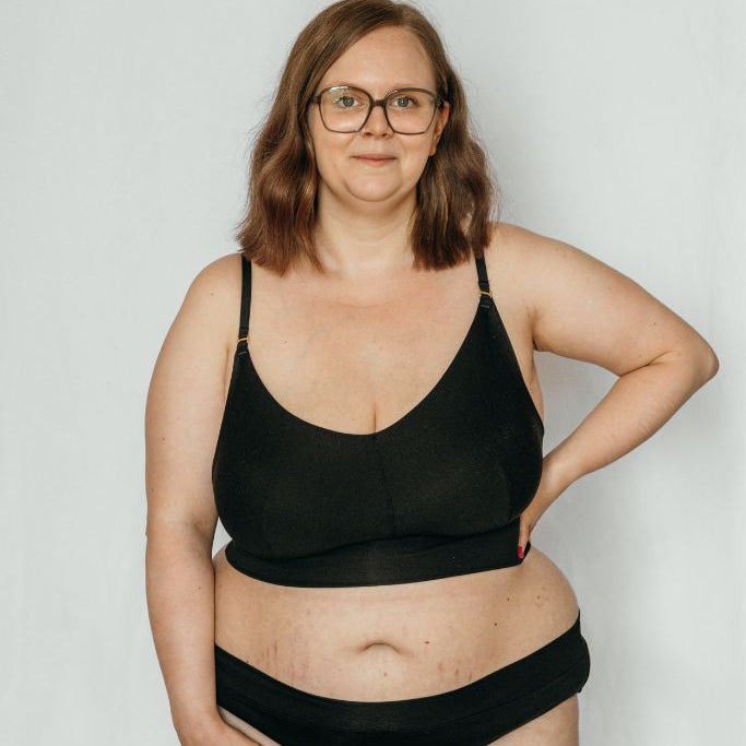 la femme à lunettes présente le Emma Mama Bralette et le Slip assorti en noir