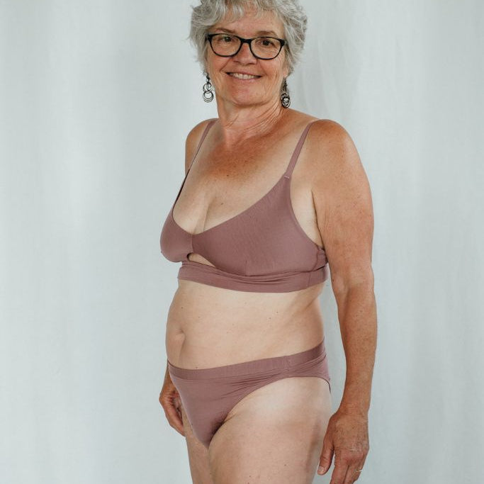 La femme regarde la caméra et porte le Thea Bralette en haut et le cheeky Slip  Thea en bas.