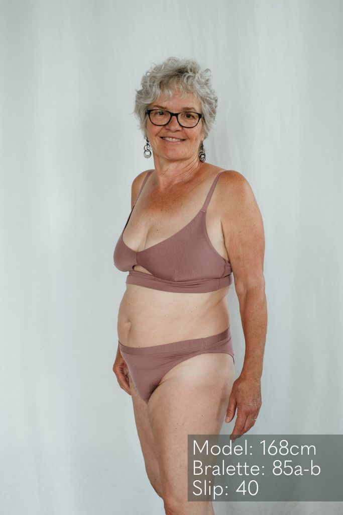 La femme regarde la caméra et porte le Thea Bralette en haut et le cheeky Slip  Thea en bas.