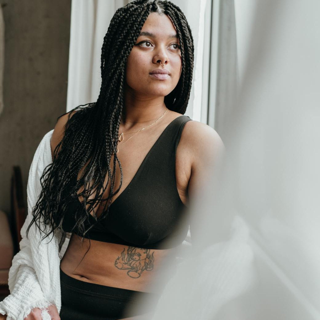 Photo romantique de modèle en lingerie noire, avec couverture blanche devant la fenêtre.