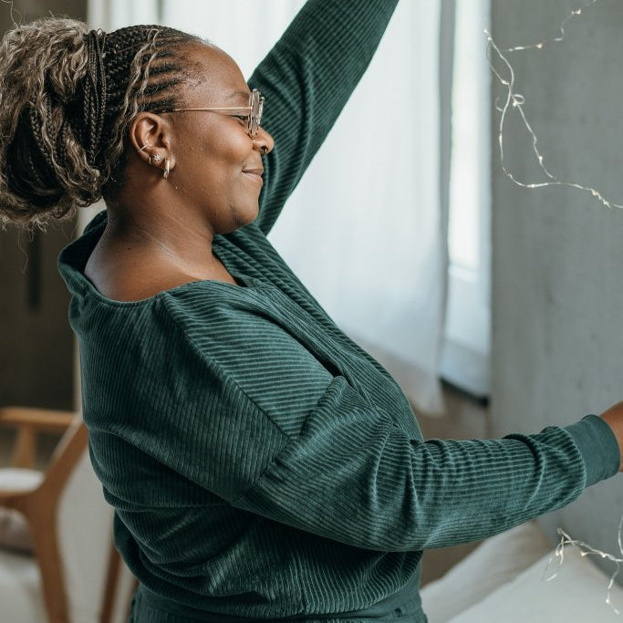 Model trägt jadegrünes Pyjama im Cord. Sie hält eine Lichterkette hoch.