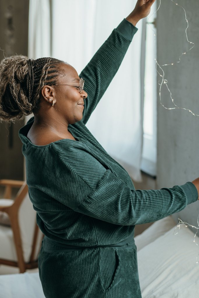 Model trägt jadegrünes Pyjama im Cord. Sie hält eine Lichterkette hoch.
