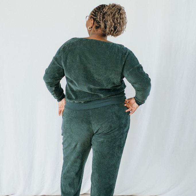 Model trägt Pyjama in jadegrünem Cord. Ihr Rücken ist der Kamera zugewandt.