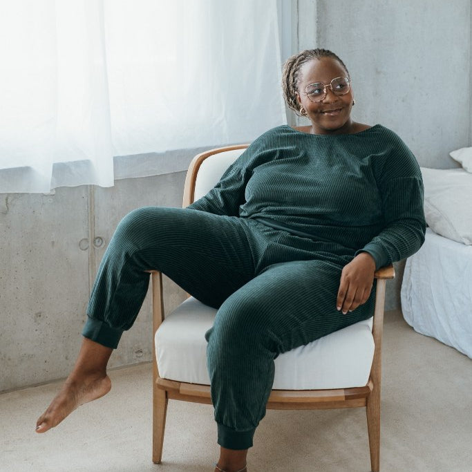 Model sitzt im jadegrünen Pyjama auf dem Sessel, ein Bein lässig über die Armlehne gelegt.