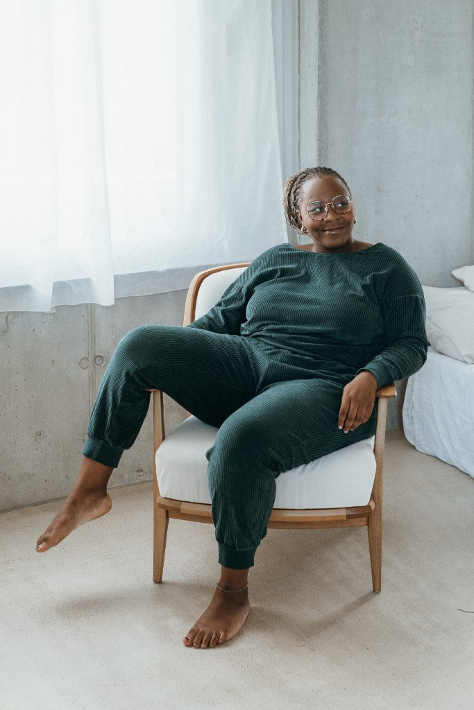 Model sitzt im jadegrünen Pyjama auf dem Sessel, ein Bein lässig über die Armlehne gelegt.