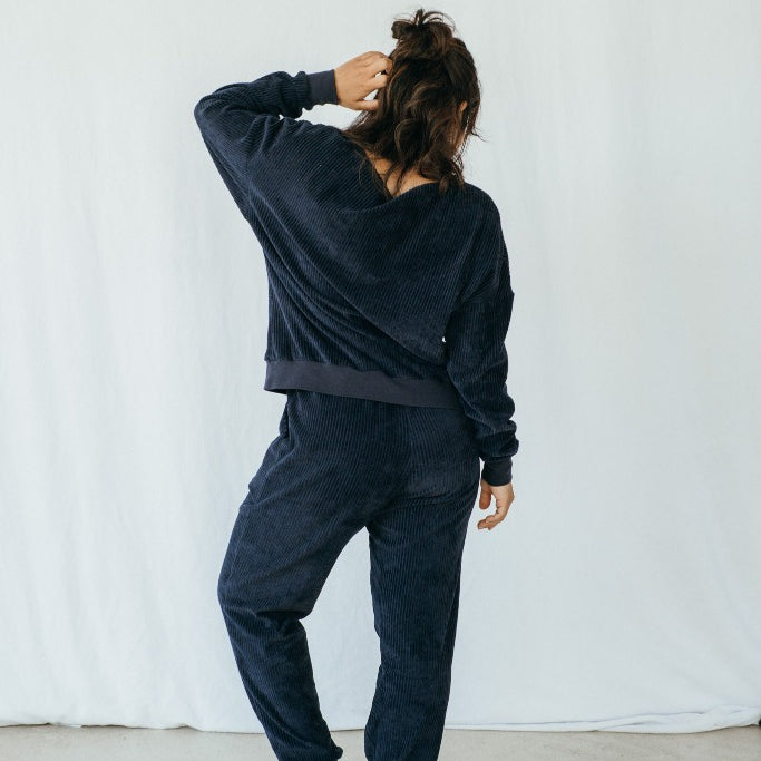 Model trägt Pyjama in Dunkelblauem Cord, ihr Rücken ist der Kamera zugewandt.