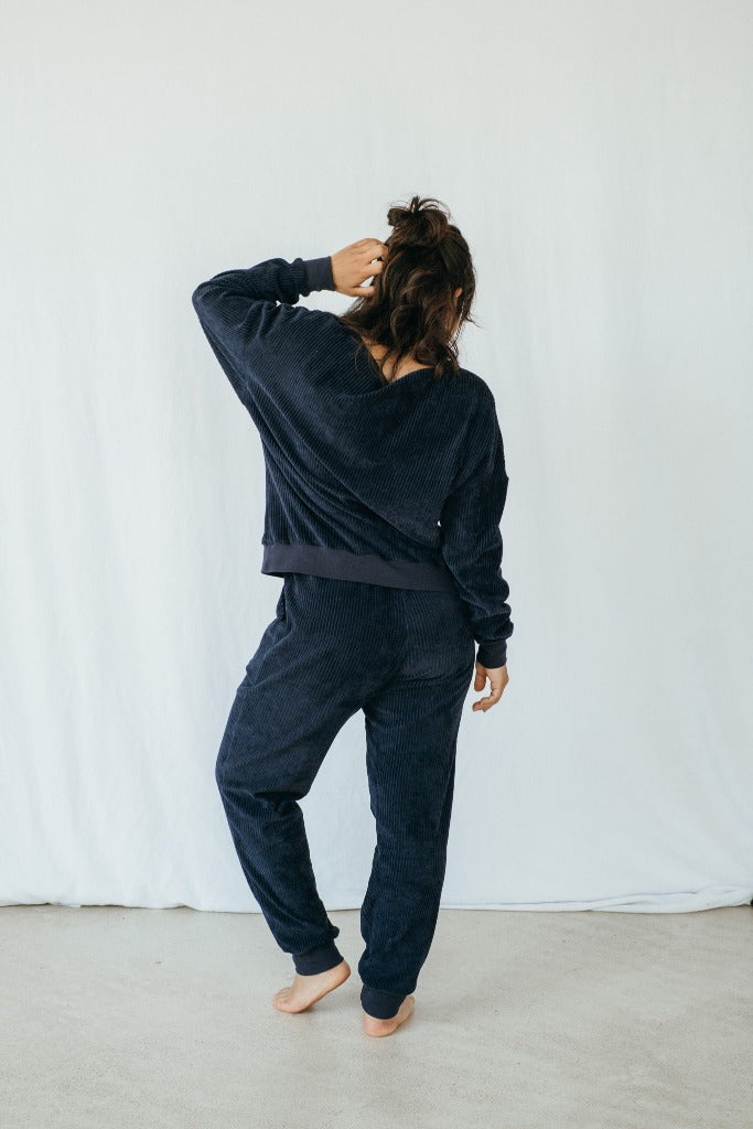 Model trägt Pyjama in Dunkelblauem Cord, ihr Rücken ist der Kamera zugewandt