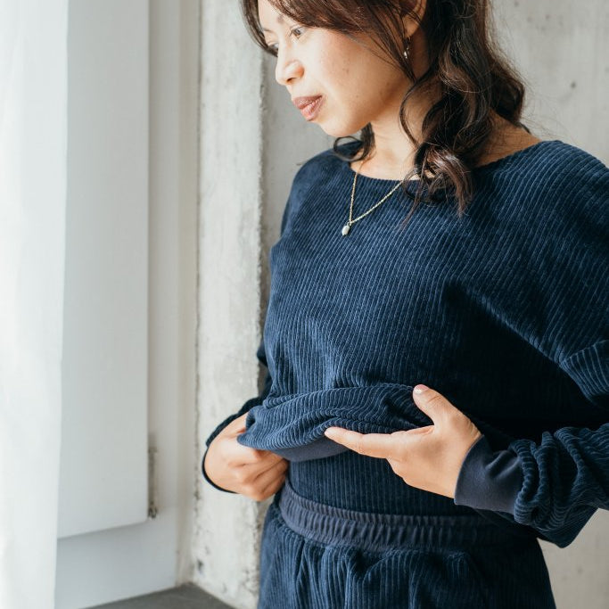 Detailaufnahme vom dunkelblauen Chloé Pullover. Das Model steht am Fenster und hebt den Pulli ganz leicht an.