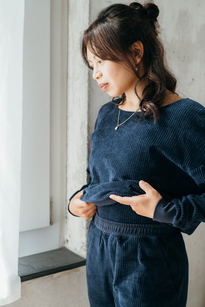 Detailaufnahme vom dunkelblauen Chloé Pullover. Das Model steht am Fenster und hebt den Pulli ganz leicht an.