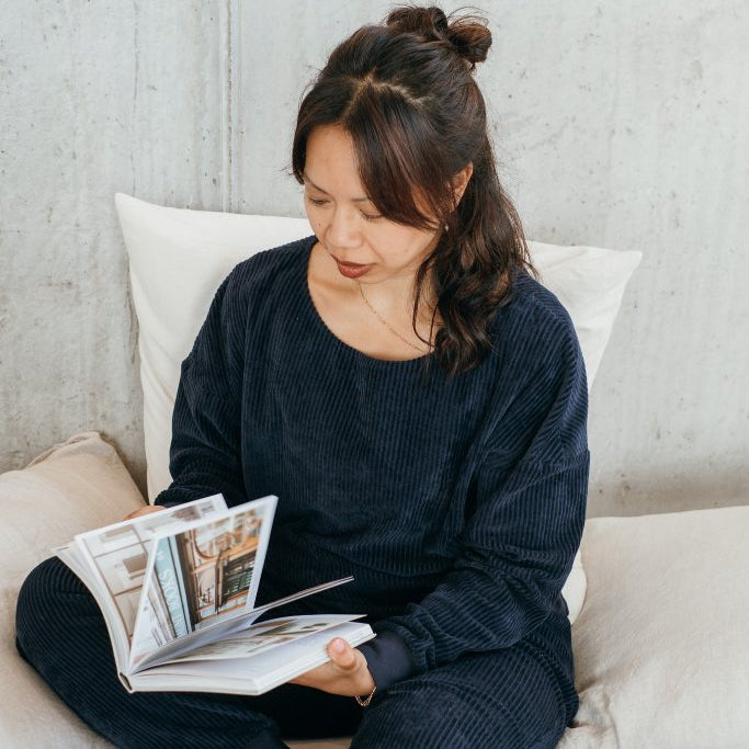 Model trägt den dunkelblauen Pyjama und liest dabei ein Buch.