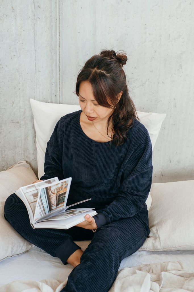 Model trägt den dunkelblauen Pyjama und liest dabei ein Buch.