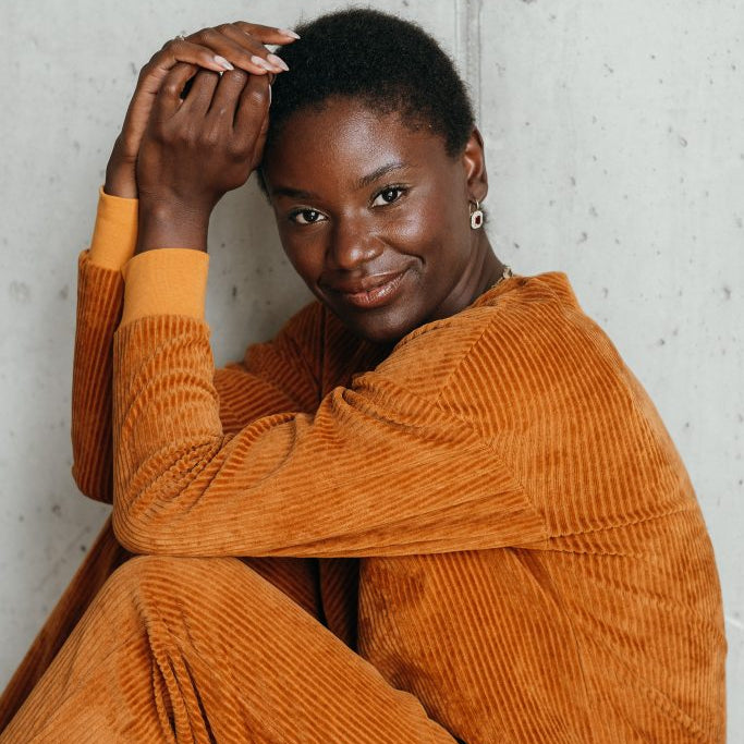 Model trägt Chloé Pullover in Ocker. Sie hat die Arme auf den Beinen angewinkelt und lächelt in die Kamera.