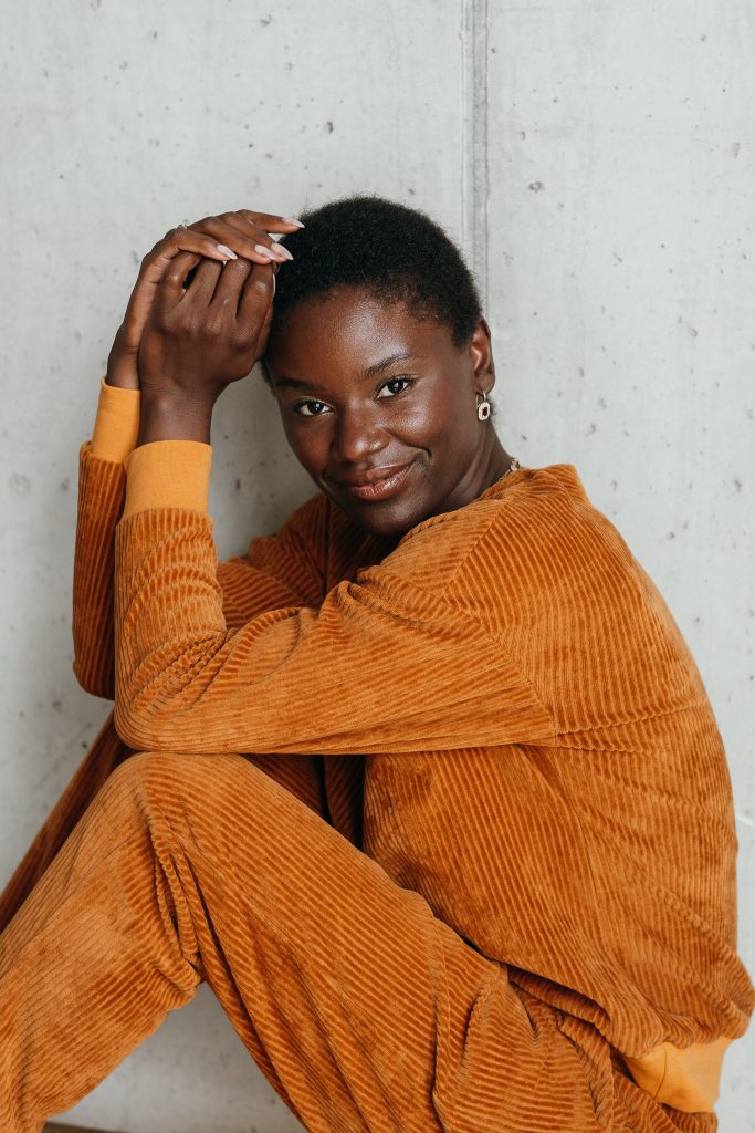 Model trägt Chloé Pullover in Ocker. Sie hat die Arme auf den Beinen angewinkelt und lächelt in die Kamera.