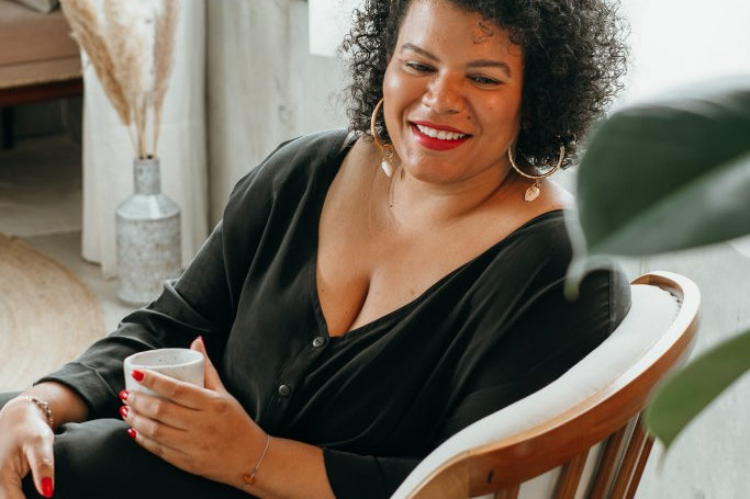 Une femme est assise dans un fauteuil et boit du café.