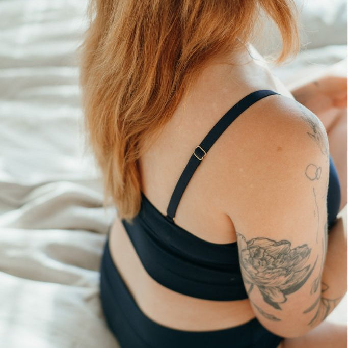 la femme est assise sur le lit et montre son épaule avec la bretelle réglable de la bralette