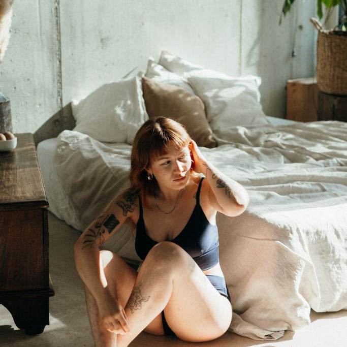 la femme est assise sur le sol et se passe la main dans les cheveux, elle porte le set de sous-vêtements Emma en bleu nuit