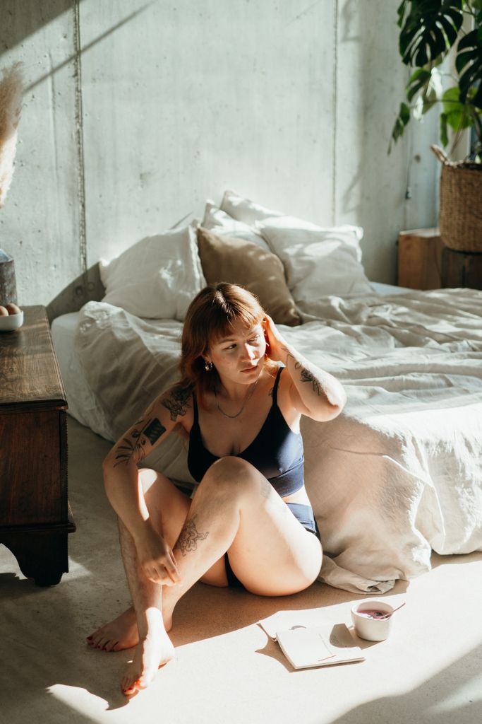 la femme est assise sur le sol et se passe la main dans les cheveux, elle porte le set de sous-vêtements Emma en bleu nuit