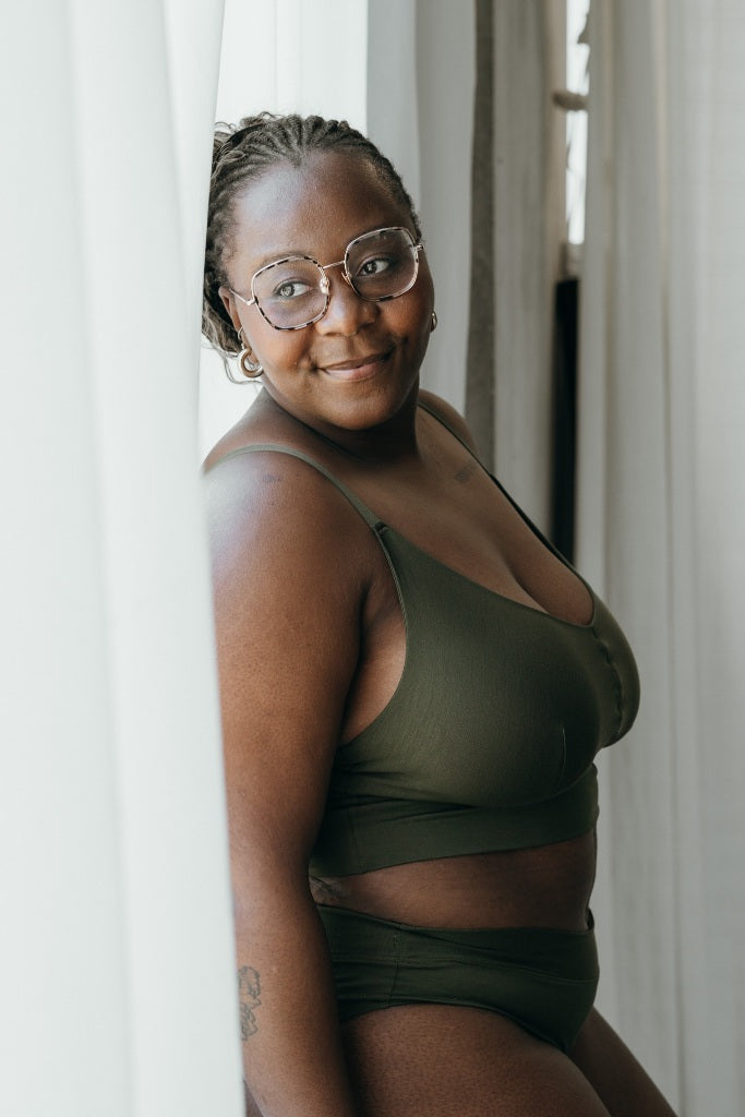 Moodbild, auf dem das Model das Emma Set in Olive trägt und gegen das Fenster lehnt