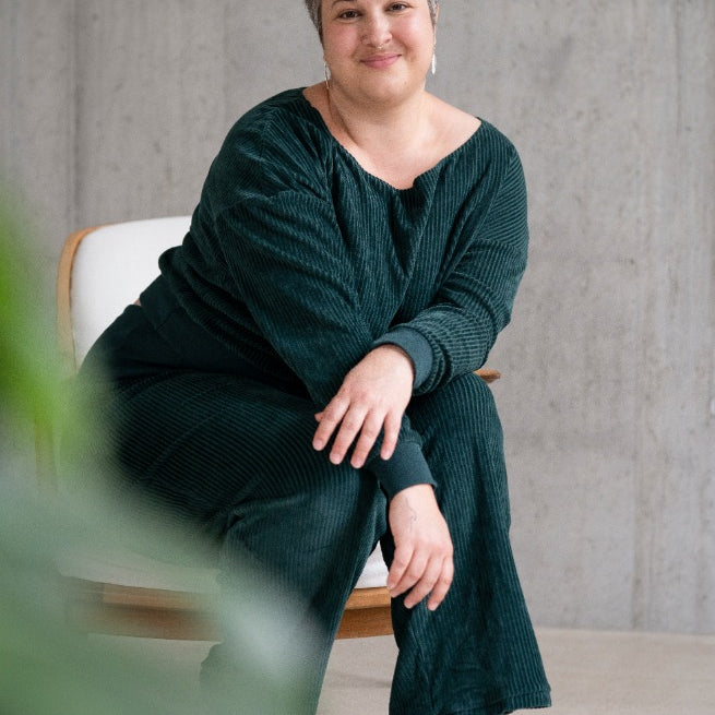 Model sitzt im jadegrünen Pyjama auf dem Sessel und lächelt direkt in die Kamera