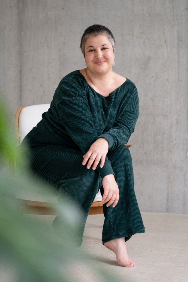 Model sitzt im jadegrünen Pyjama auf dem Sessel und lächelt direkt in die Kamera