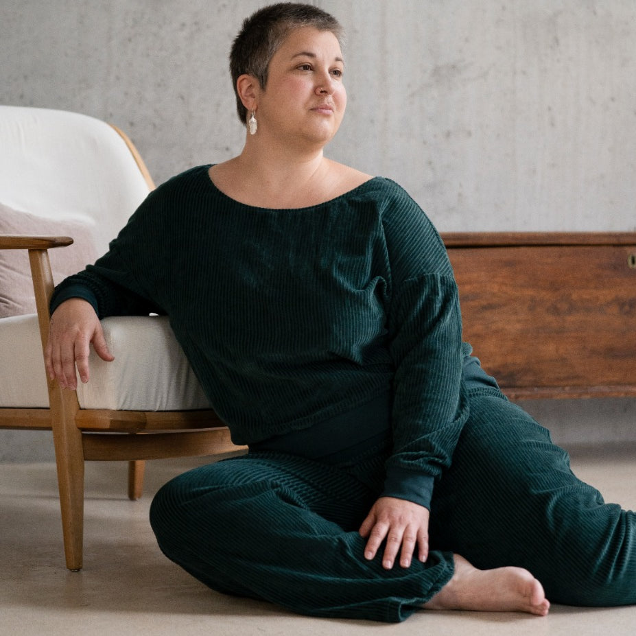 Model sitzt im jadegrünen Pyjama auf dem Boden, lässig auf einem Sessel abgestützt