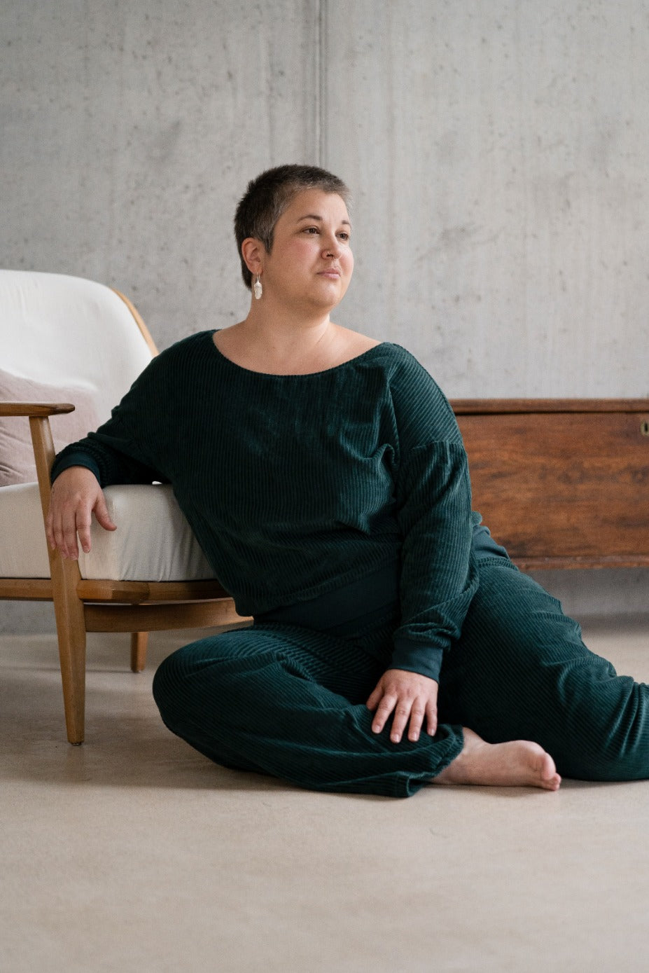 Model sitzt im jadegrünen Pyjama auf dem Boden, lässig auf einem Sessel abgestützt